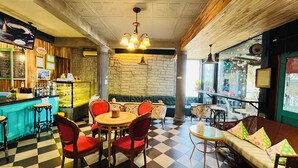 A cozy cafe with checkered flooring, a bar area, and a seating area with red chairs and a sofa. - Lenoi Buri (Khuan Khanun)
