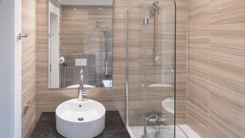 A modern bathroom with a round sink, a glass-enclosed shower, and a mirror above the sink.