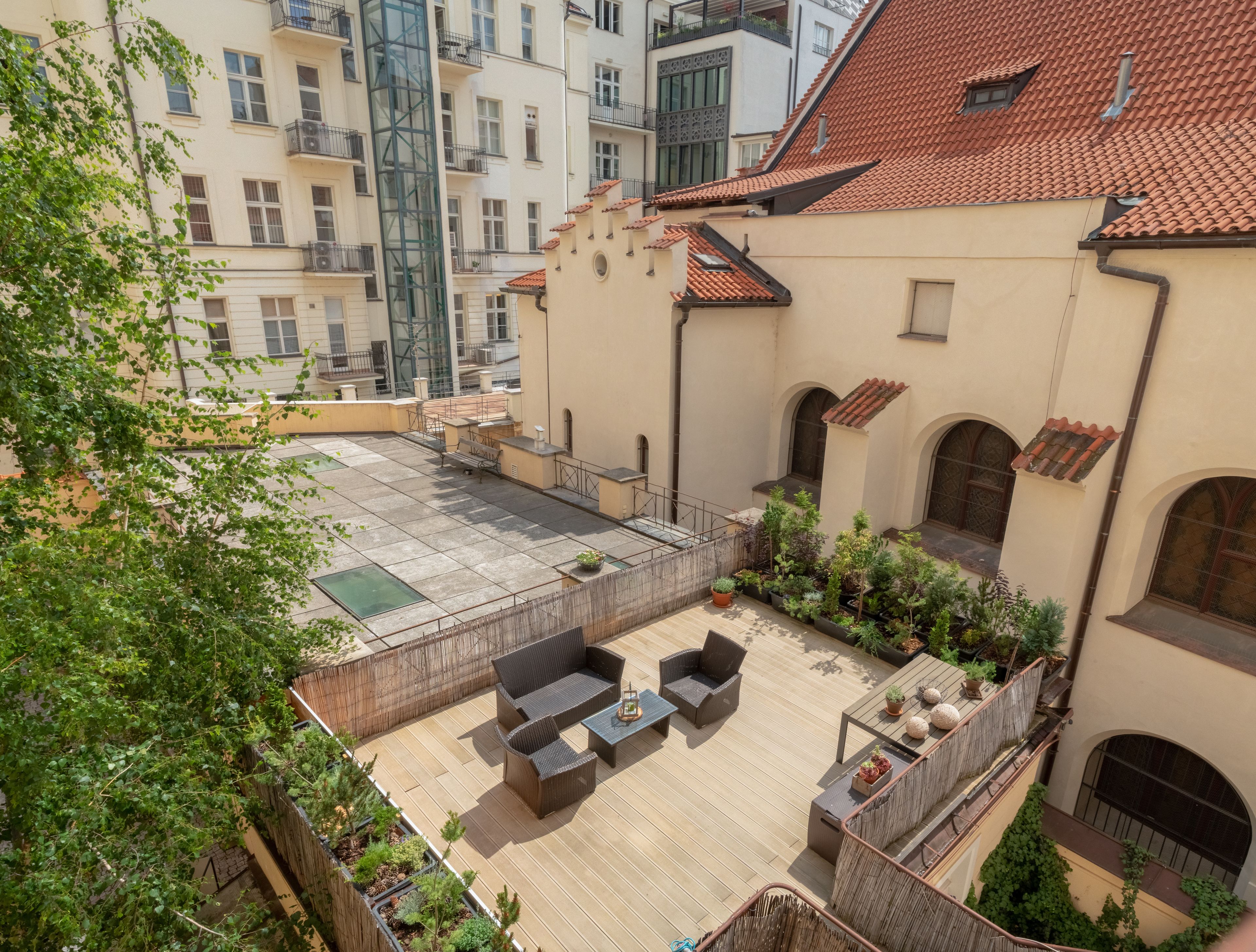 A rooftop terrace with outdoor seating, a small garden area, and a view of surrounding buildings.