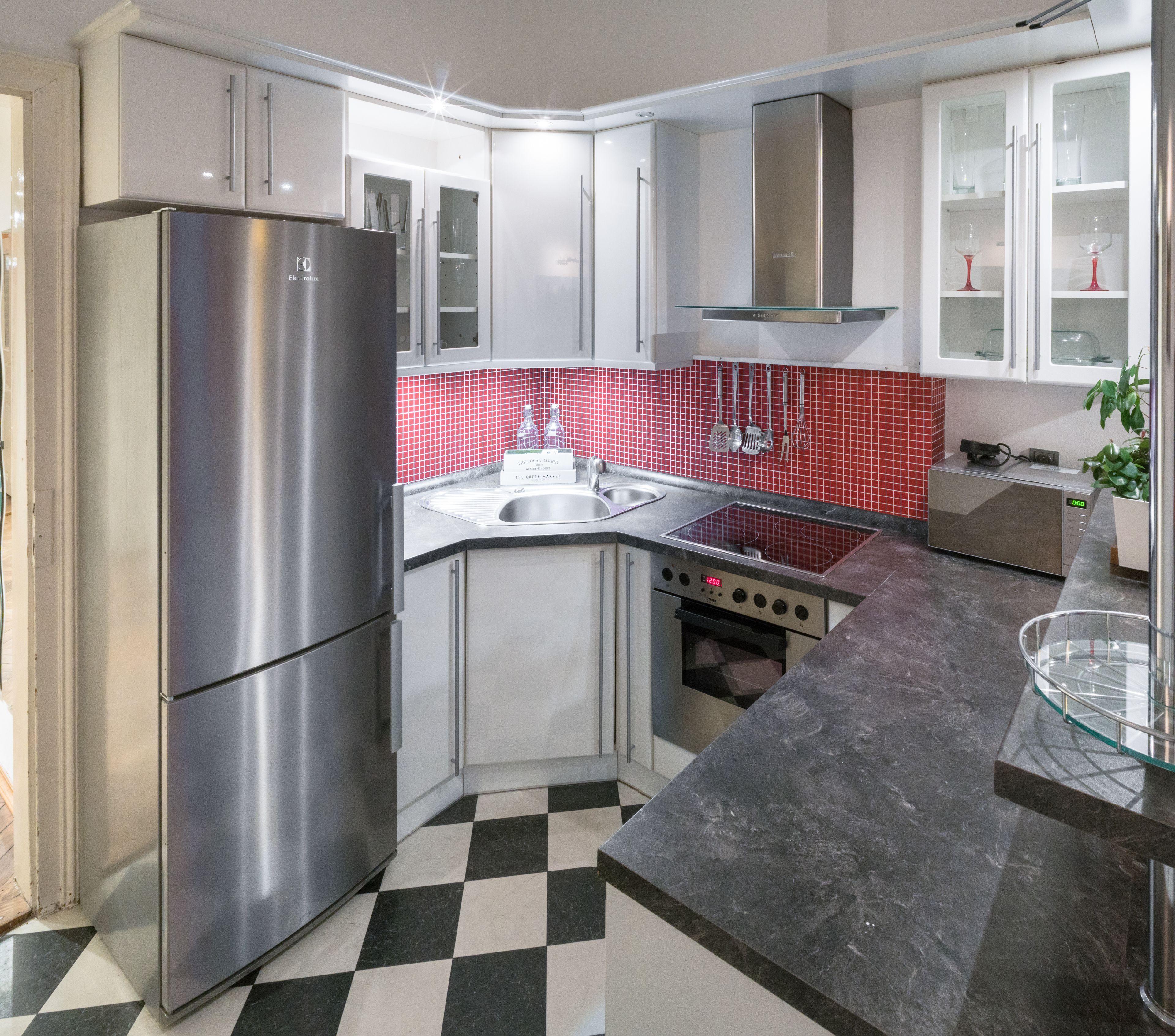 Una cucina moderna con elettrodomestici in acciaio inossidabile, pavimento a scacchi e zoccolo posteriore in piastrelle rosse.