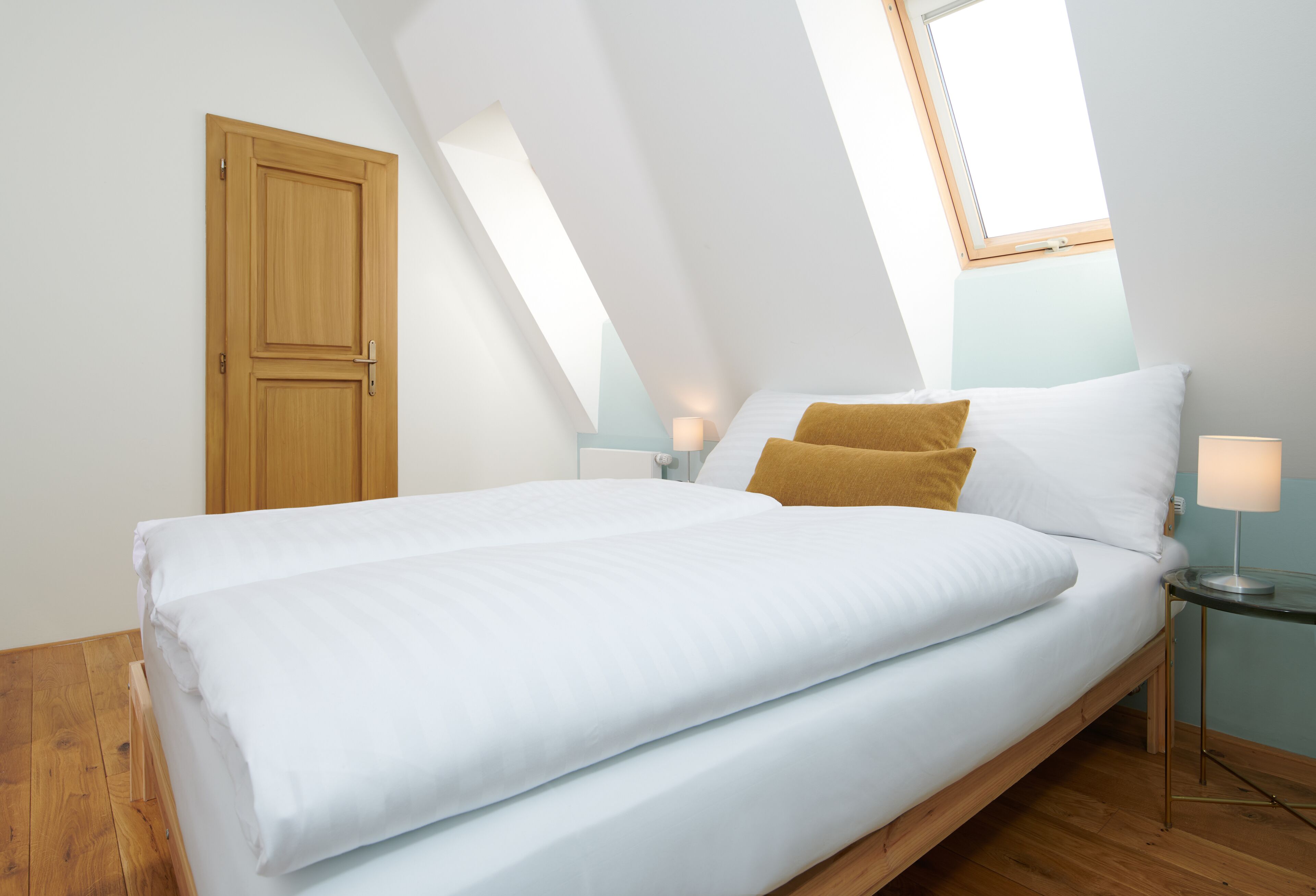 A bedroom with a bed, a wooden door, a nightstand, and a lamp.