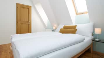 A bedroom with a bed, a wooden door, a nightstand, and a lamp.