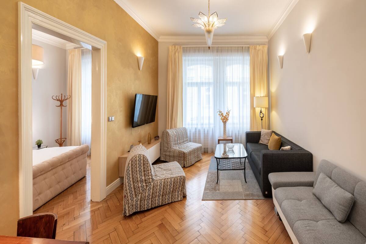 A living room with a sofa, armchairs, a coffee table, and a TV mounted on the wall.