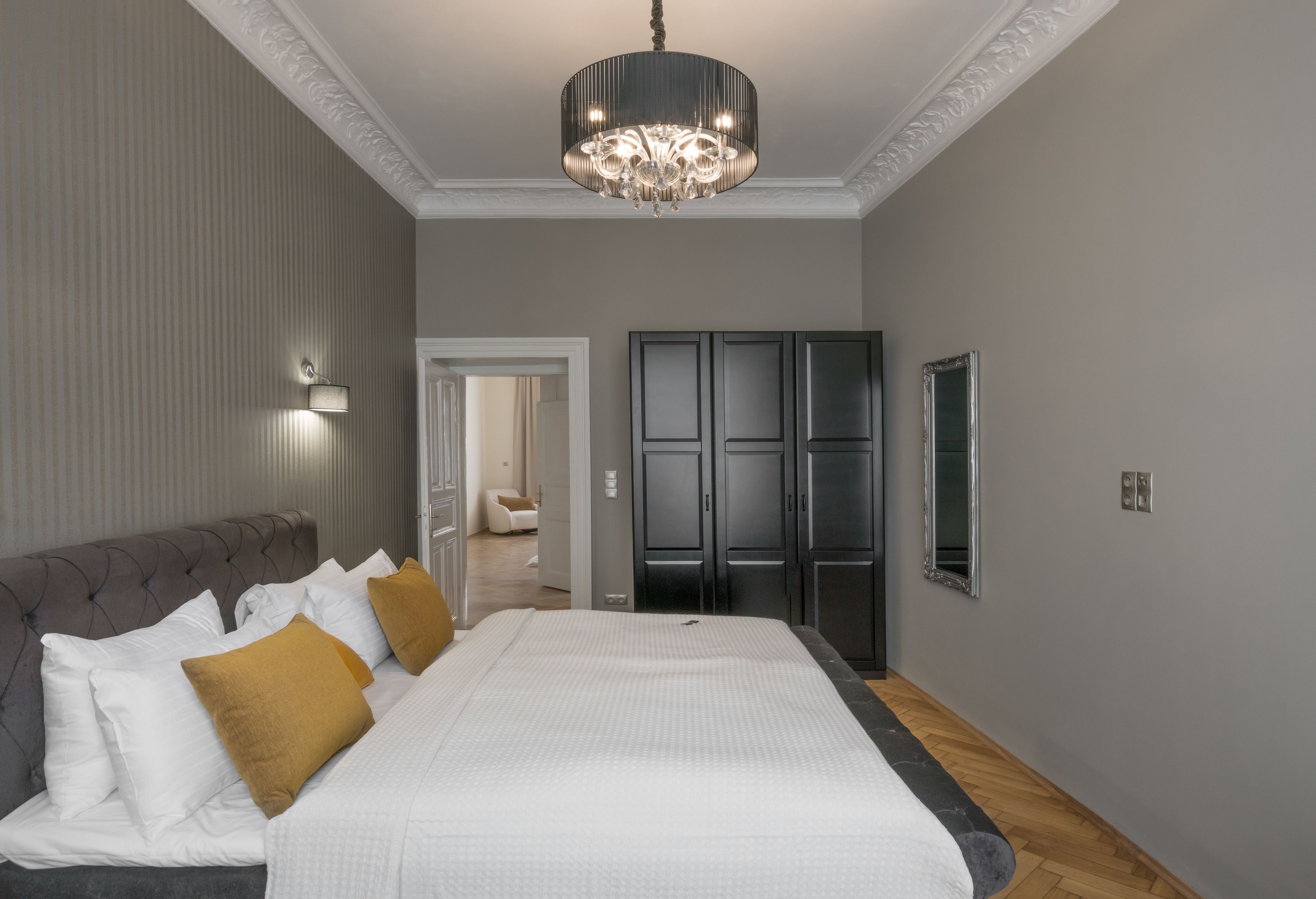 A bedroom with a large bed, a chandelier, a wardrobe, and a mirror.