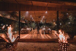 Un espace extérieur aménagé pour les repas, avec un sol en bois, des tables, des chaises et des plantes en pot.