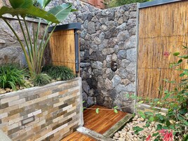 Un mur de pierre surmonté d’une clôture en bambou, une porte en bois et une petite plateforme en bois.