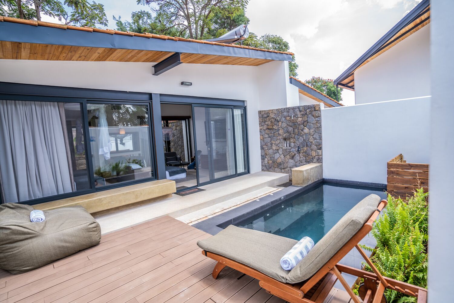 A modern outdoor pool area with a wooden deck, lounge chairs, and a stone wall.