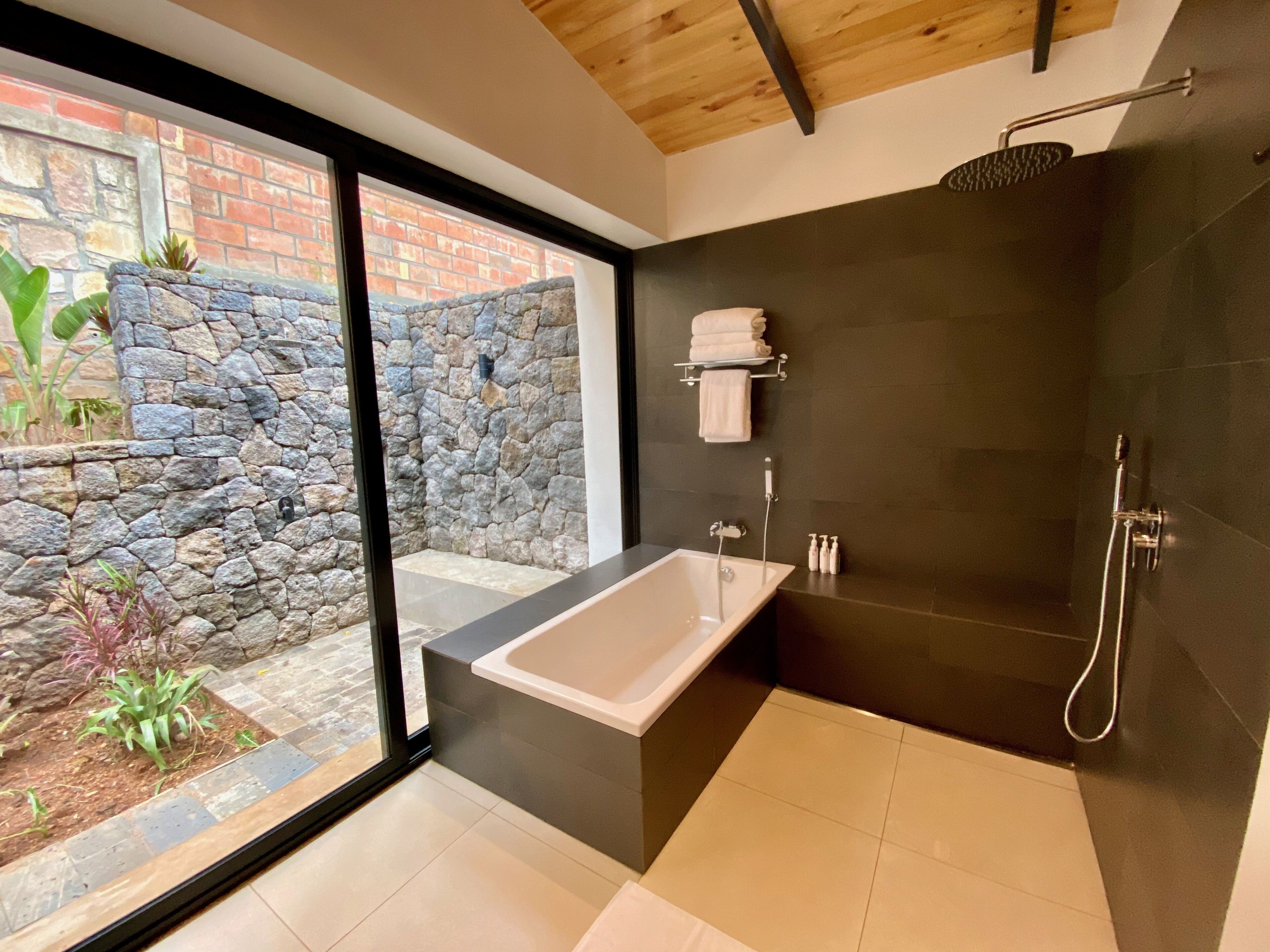 A modern bathroom with a freestanding bathtub, a shower, and a stone wall.