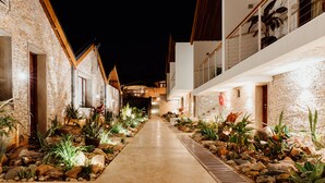 A nighttime view of a building with a stone facade, a concrete pathway, and various plants. - Hemingways Retreat Kigali (Kigali)