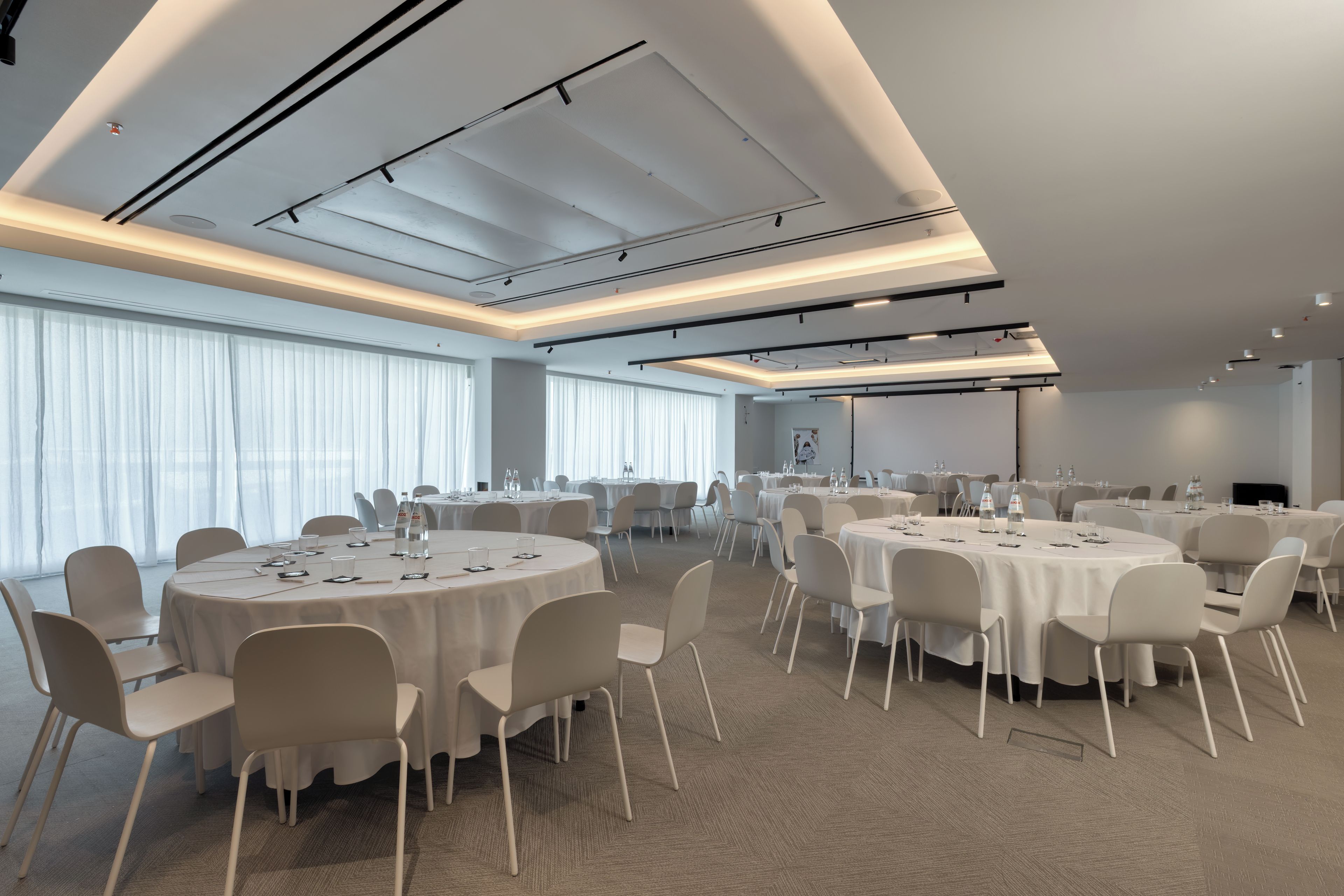 Une salle de conférence avec des tables rondes, des chaises blanches et un sol recouvert de moquette.