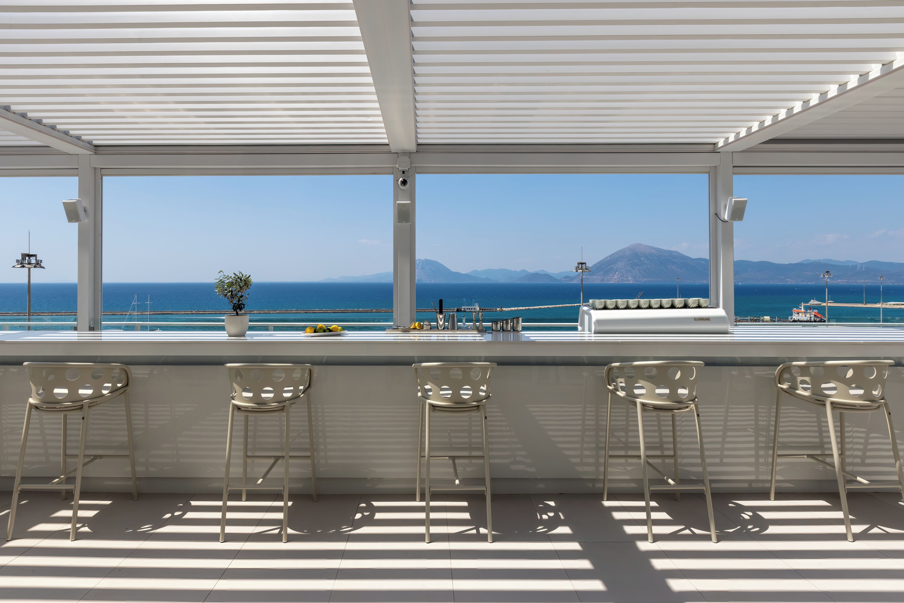 Un bar lumineux, baigné de soleil, avec vue sur la mer et les montagnes.
