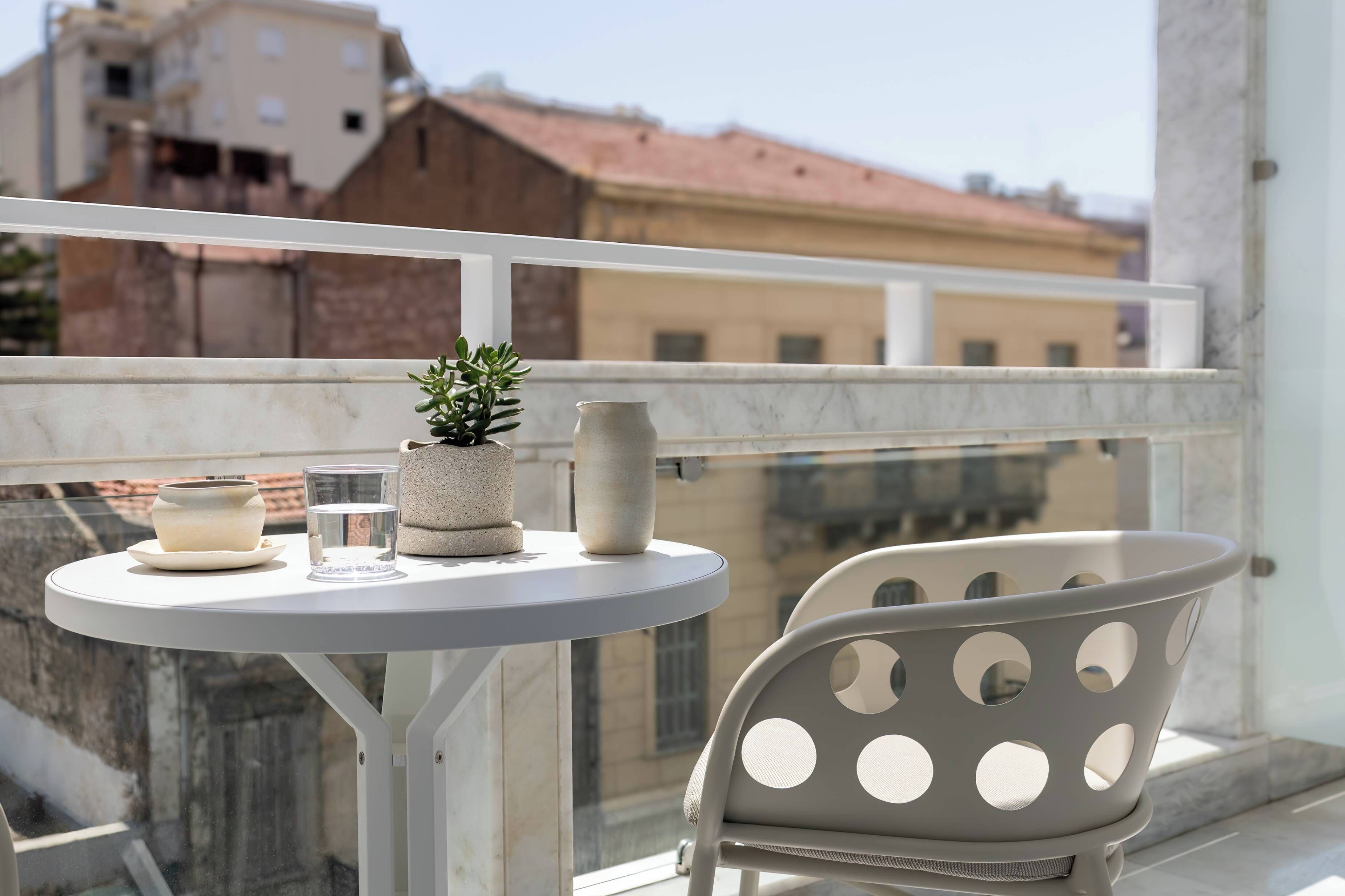 Un balcón con una mesa redonda, una planta en maceta, una vela y un vaso de agua.