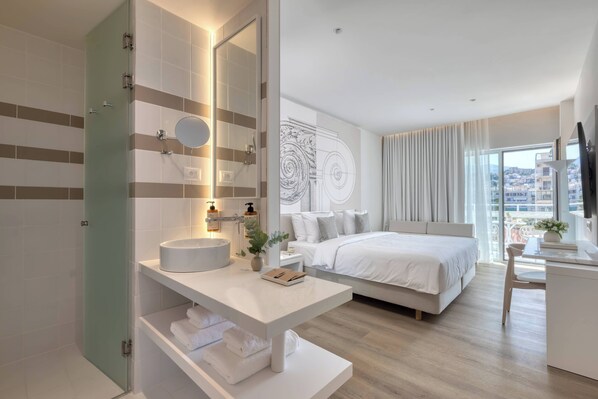 A modern hotel room with a large bed, a bathroom with a vanity, and a city view. - Mercure Patras Astir (Patras)