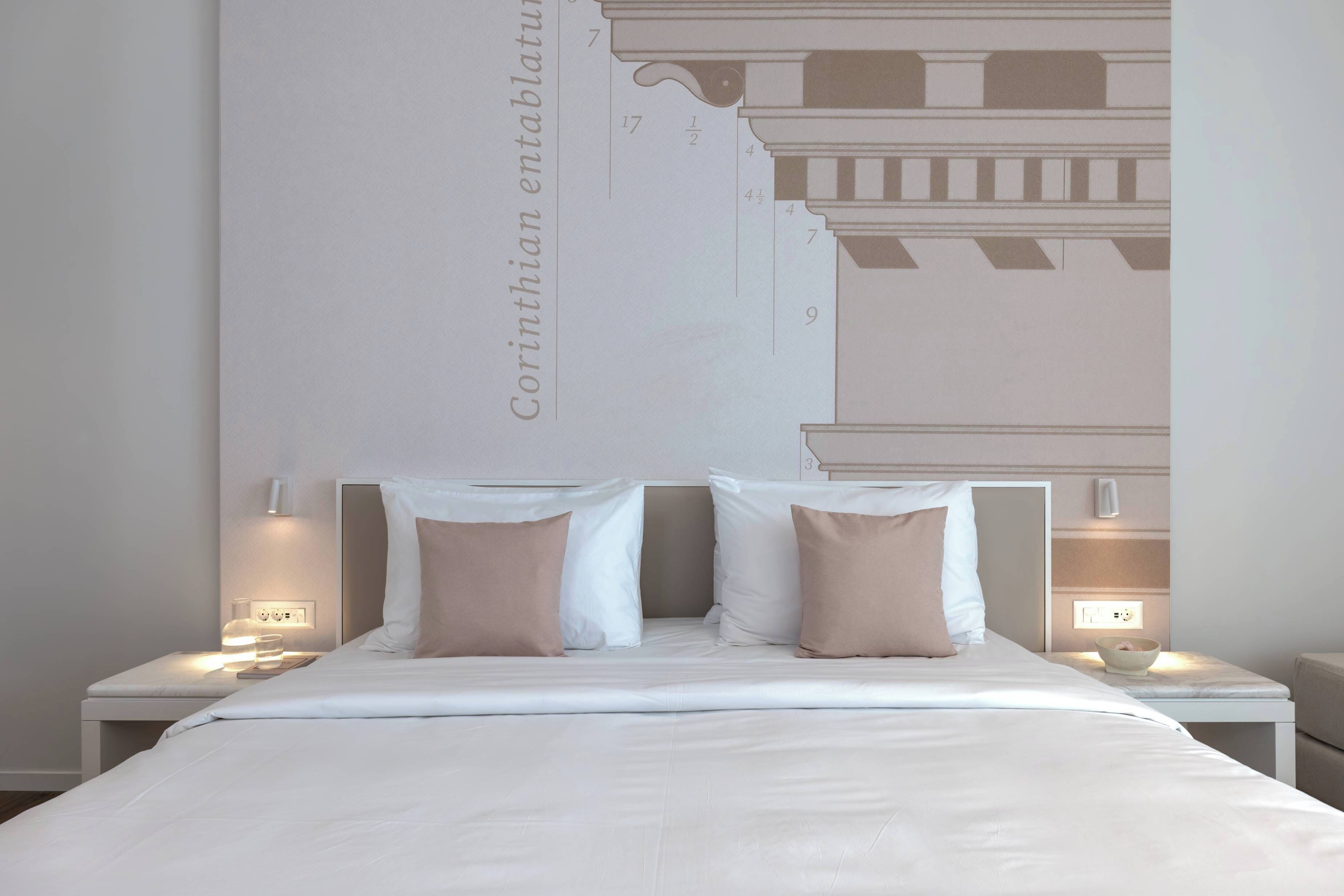 Quarto com uma cama grande, duas mesas de cabeceira e luminária na parede.
