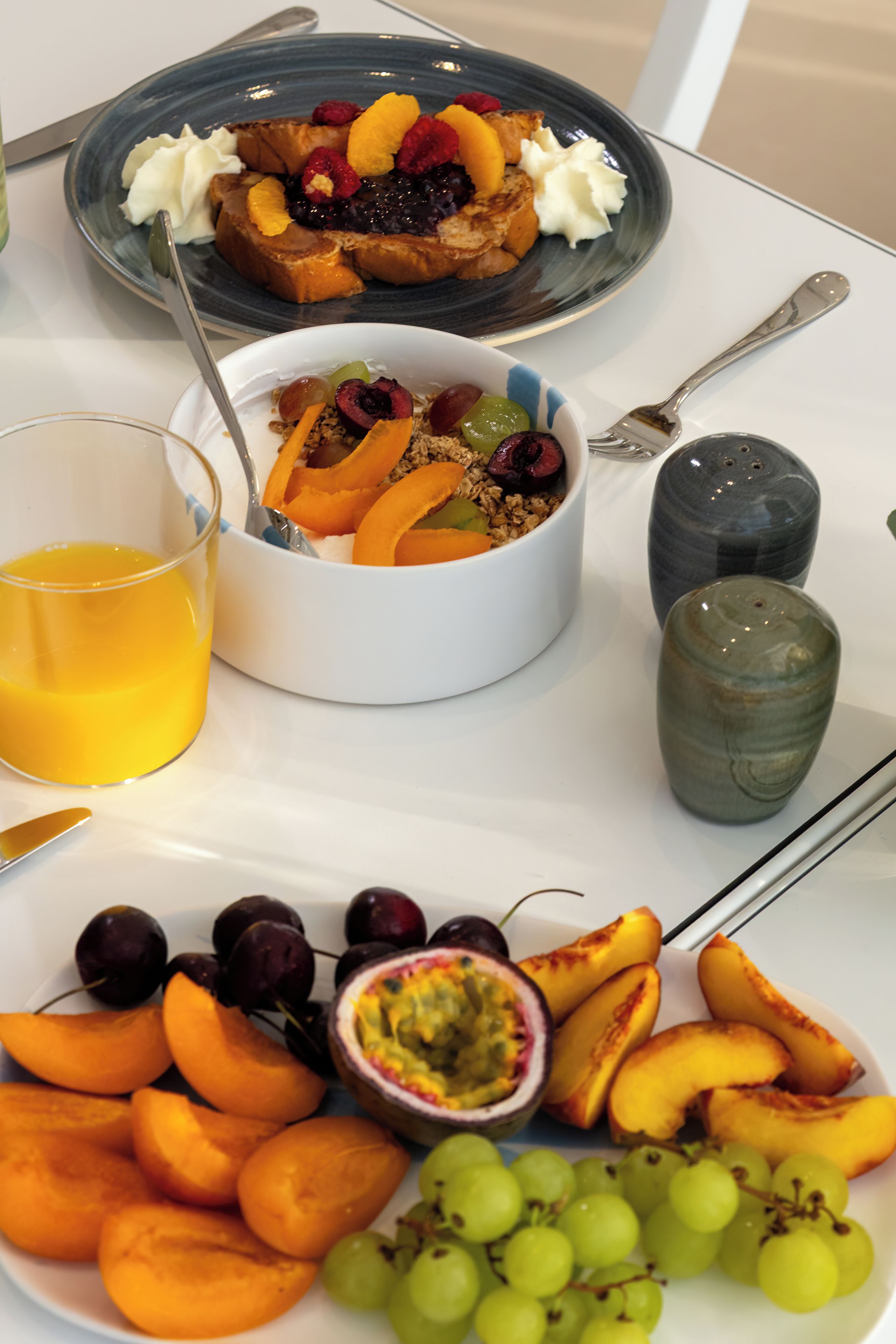 A breakfast setting with a plate of fruit, a bowl of cereal, and a glass of orange juice.