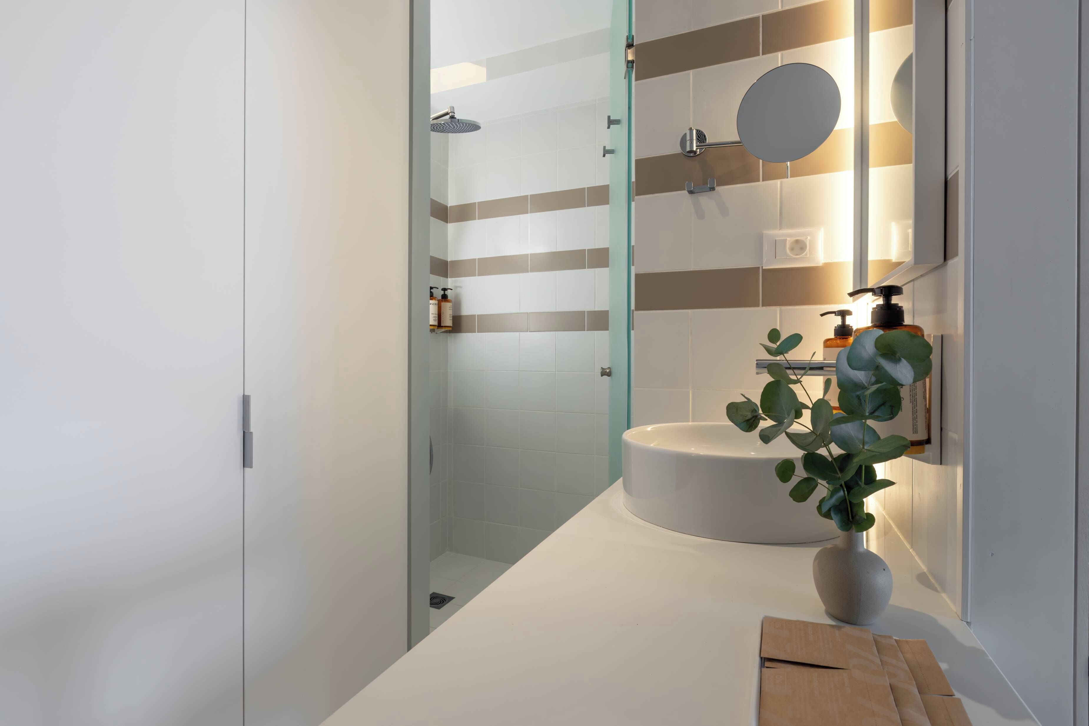 Een moderne badkamer met een douchecabine van glas, een witte wastafel en een spiegel met een ronde lijst.