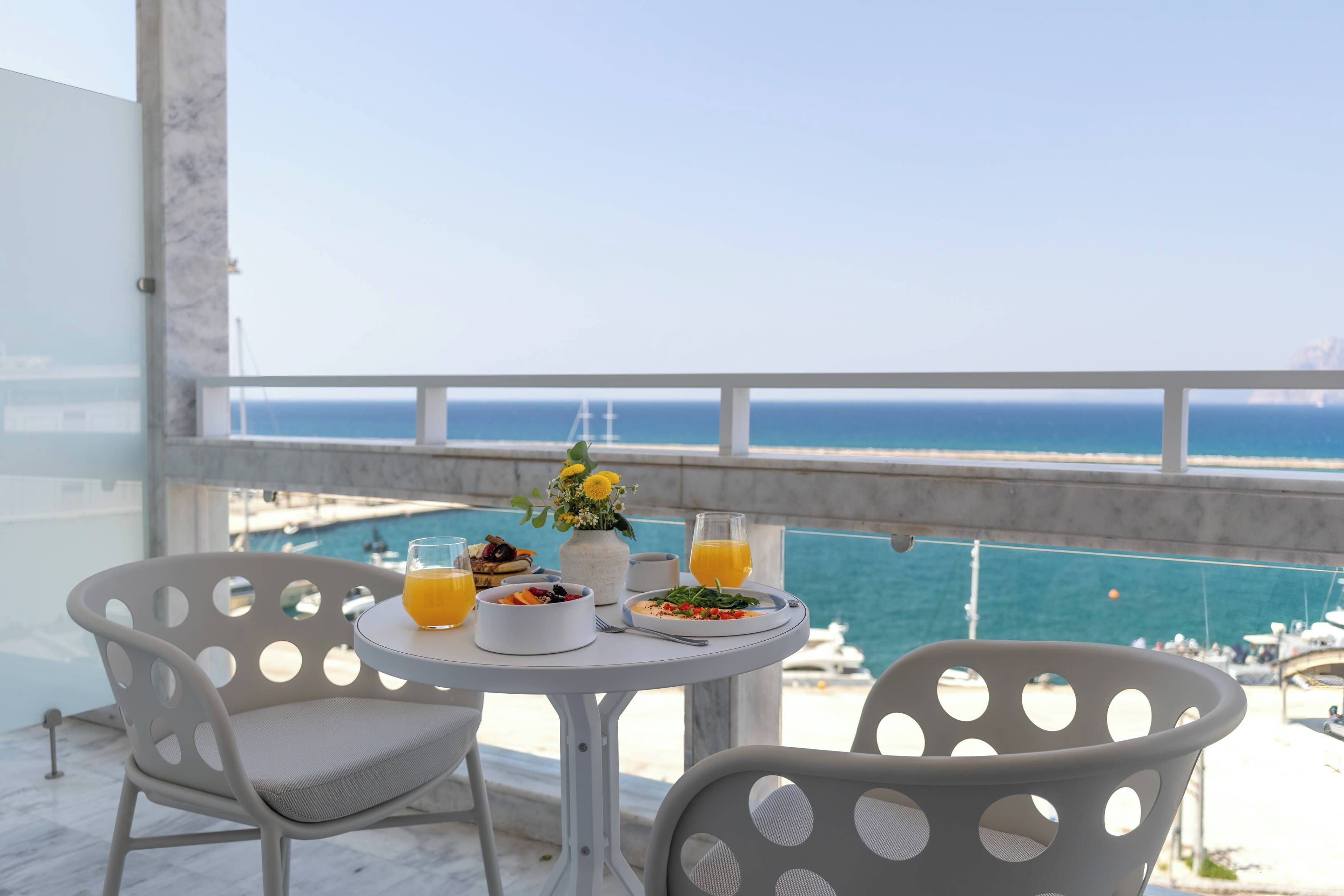 Un balcón con una mesa dispuesta para el desayuno, con vista a un puerto deportivo y al mar.