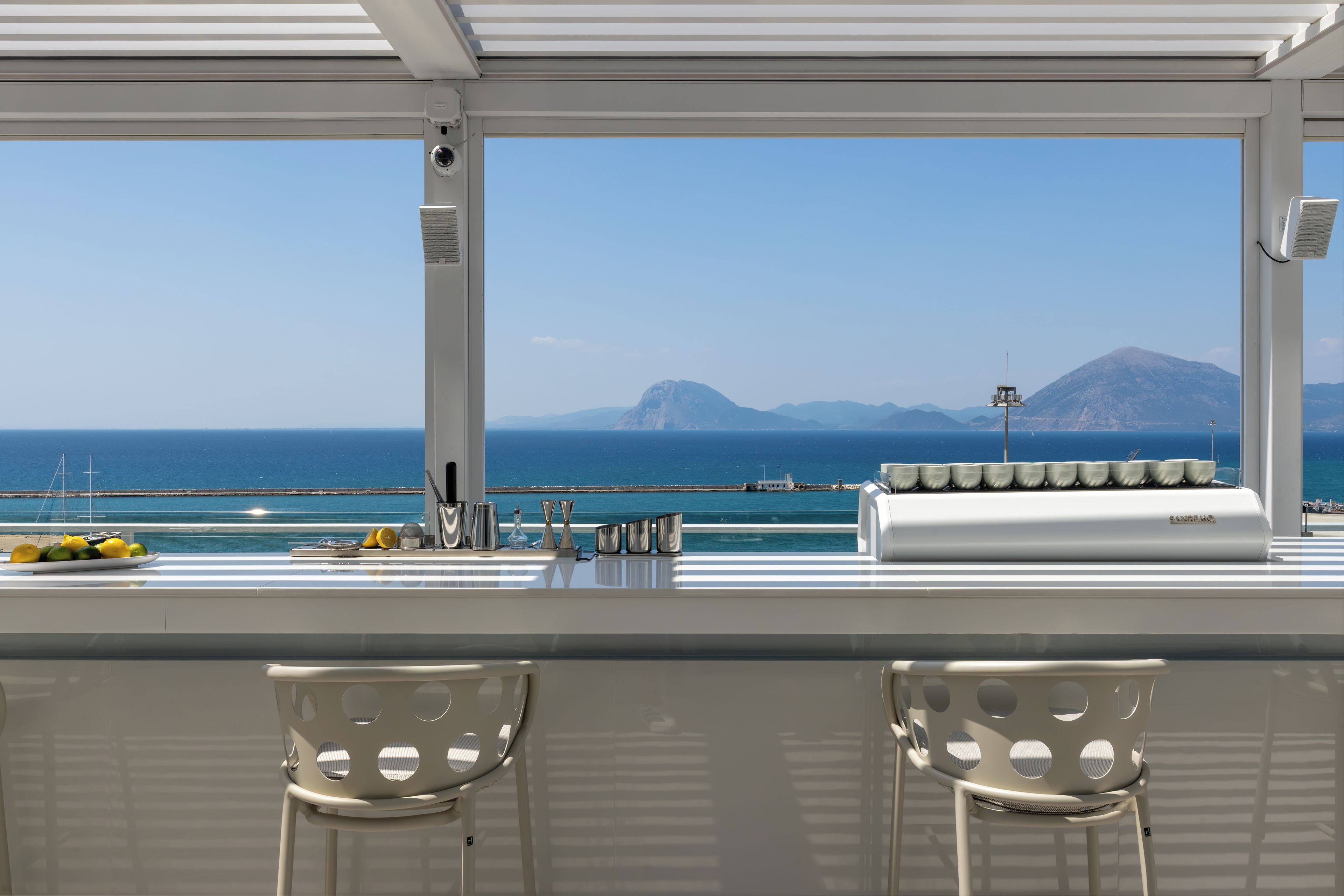 A bar area with a view of the sea and mountains, equipped with bar stools and a counter.