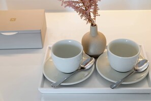 Two white cups on a tray with spoons, a vase with dried flowers, and a white box in the background. - Mercure Patras Astir (Patras)