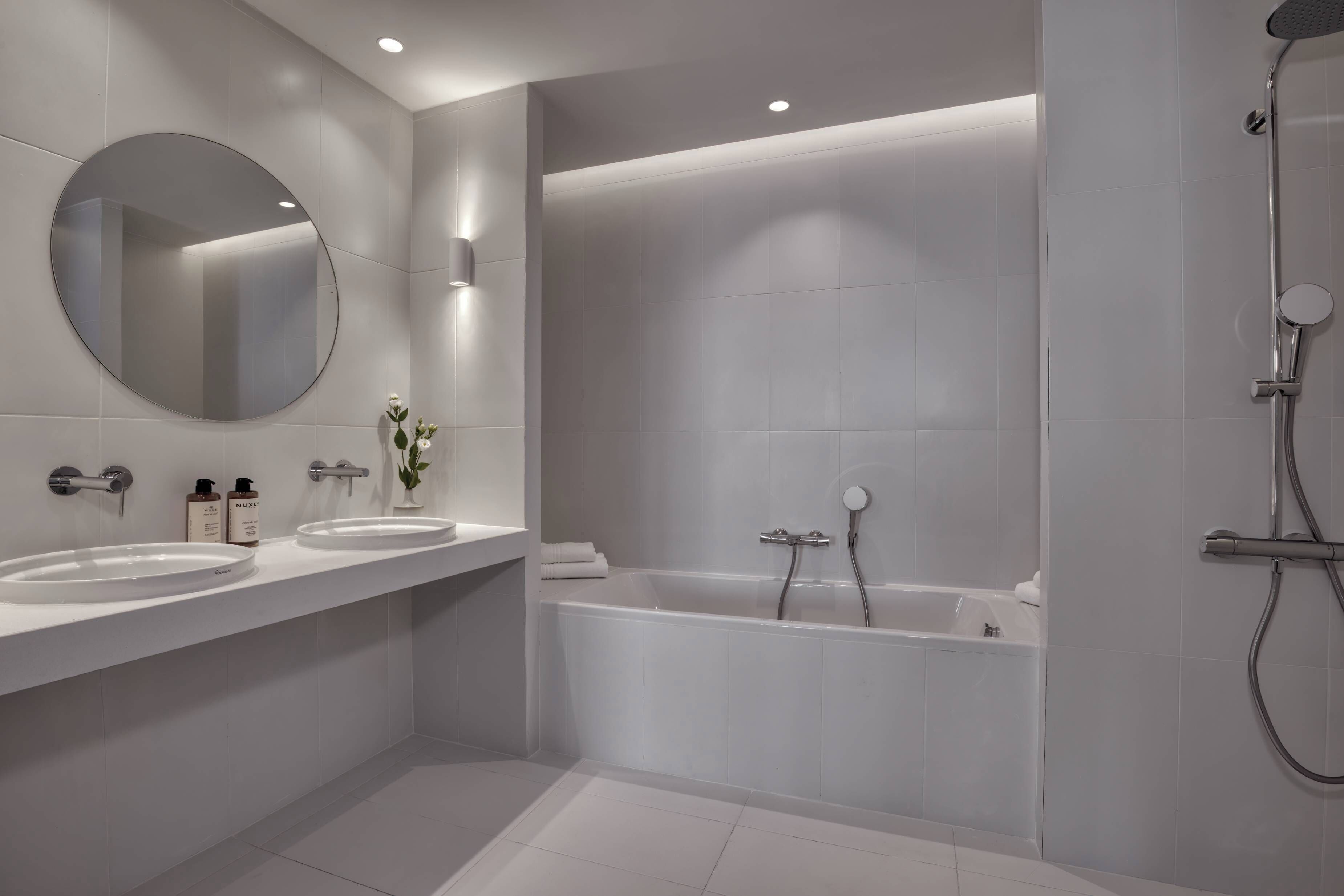 Un baño moderno con dos lavamanos, un espejo grande, una bañera y una ducha.