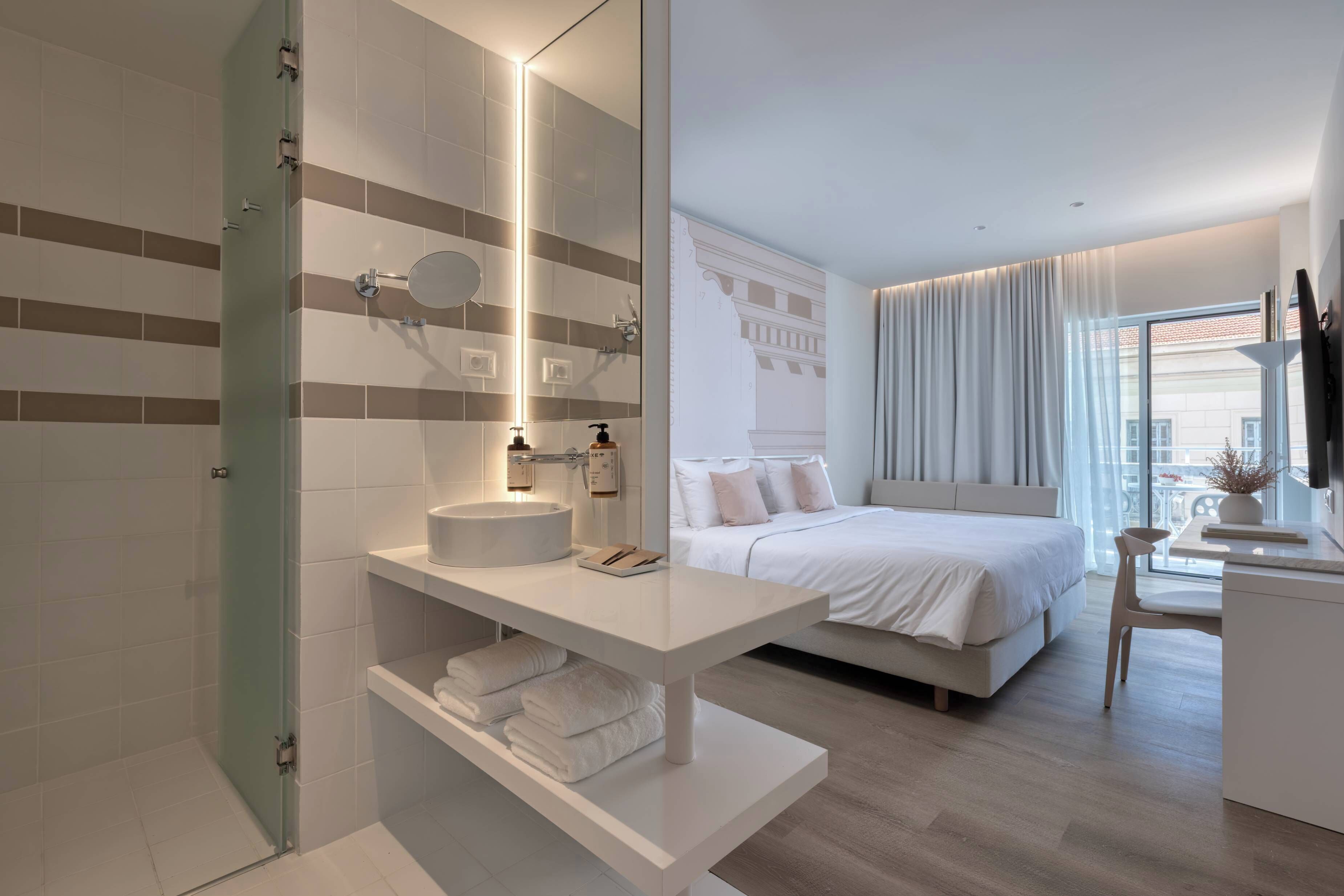 A modern hotel room with a large bed, a bedside table, a bathroom with a round sink, and a large window.
