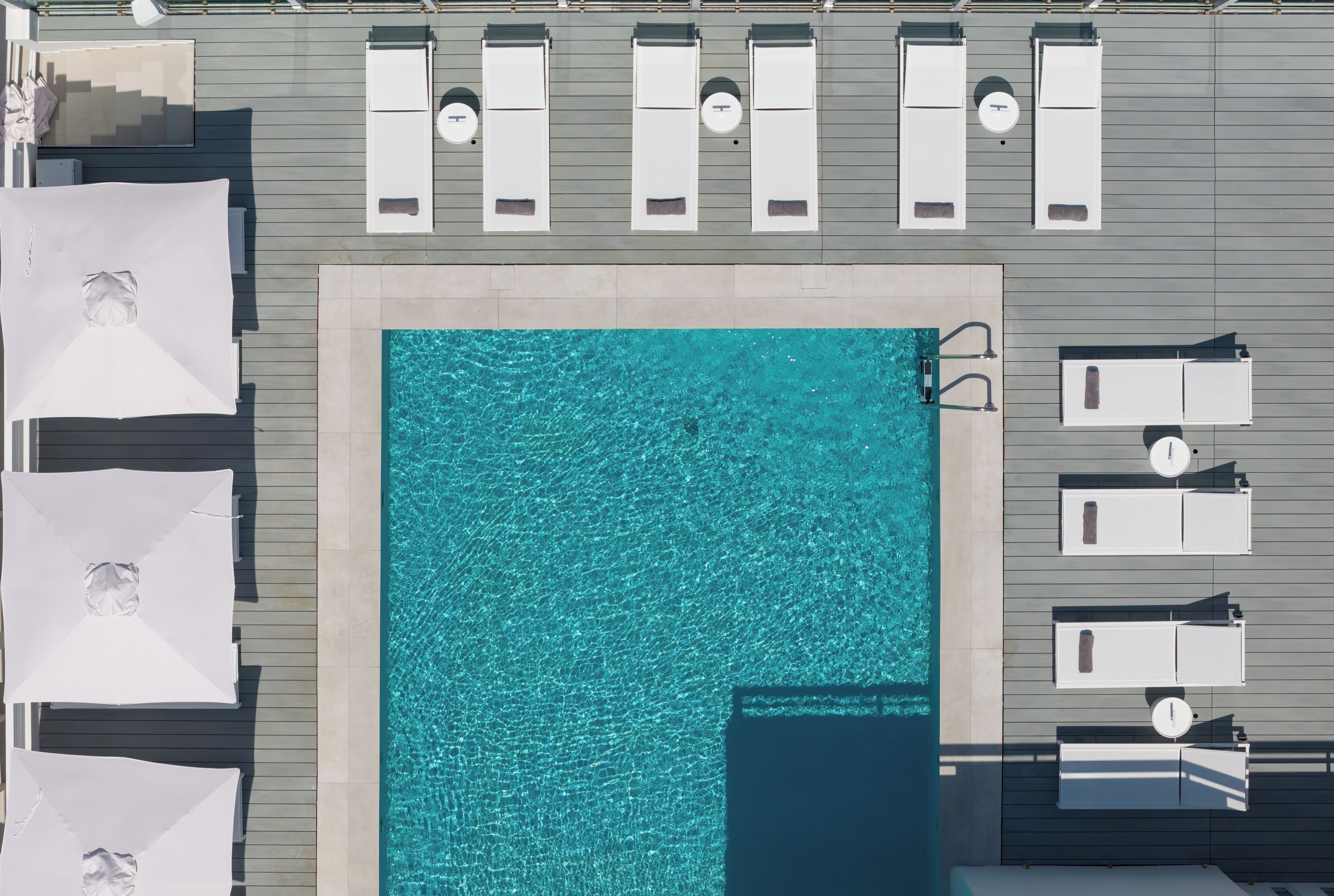 An aerial view of a rooftop pool area with multiple sun loungers and a swimming pool.