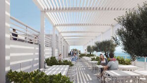 Un área de estar al aire libre con mesas y sillas blancas, una pérgola encima y vista al mar.