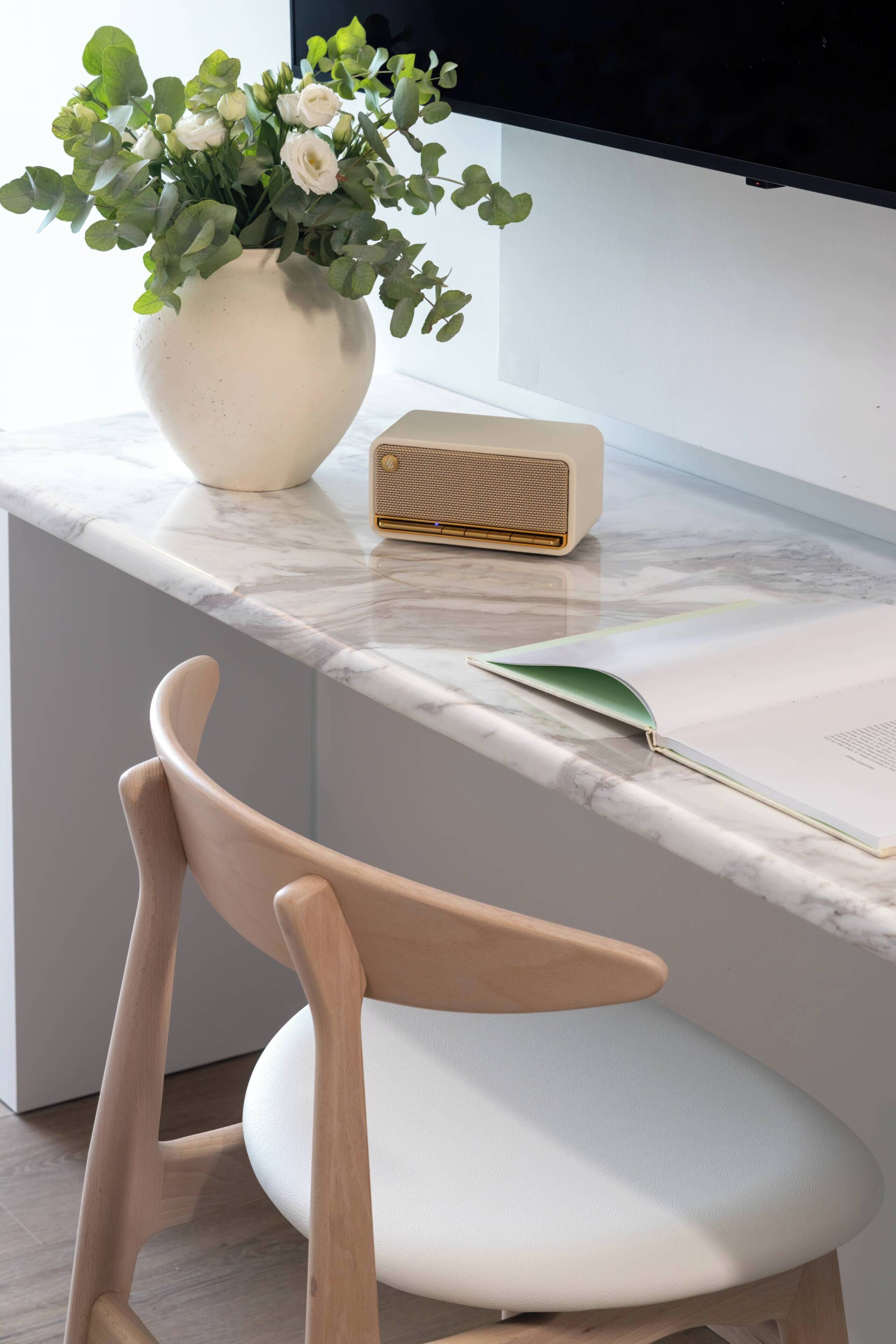 Una cocina moderna con encimera de mármol, un florero blanco con flores, una radio antigua y una silla de madera.