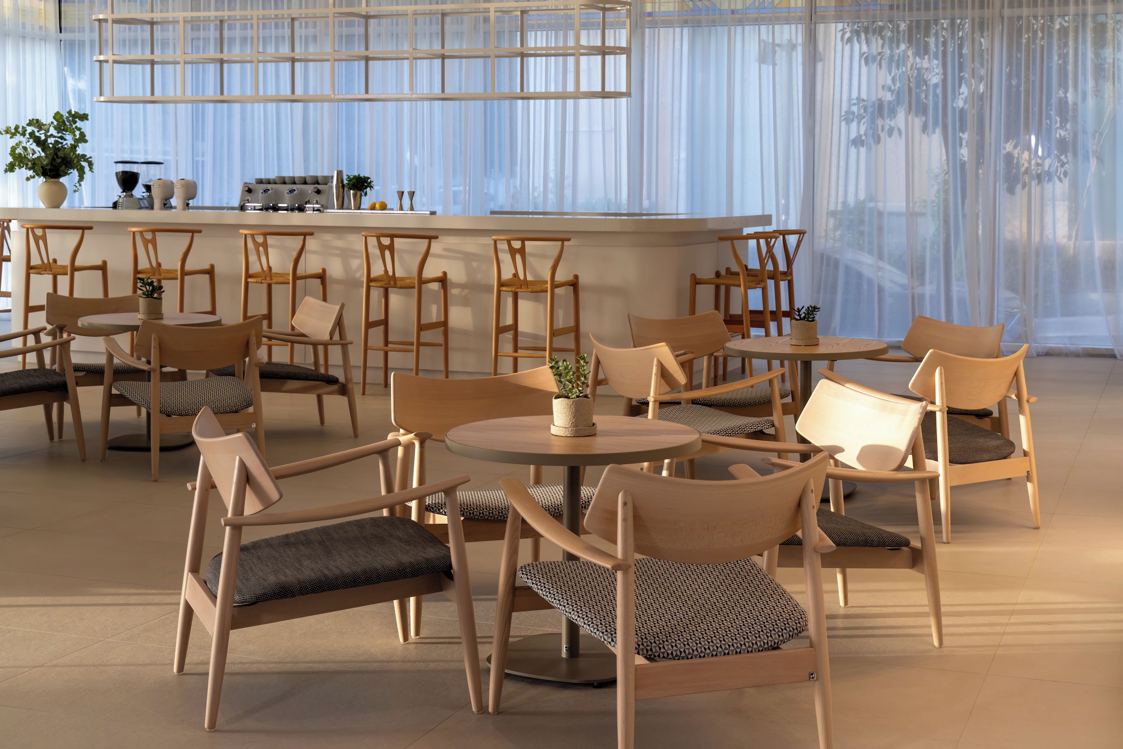 Um interior moderno com área de bar, diversos assentos e vista através de cortinas leves.