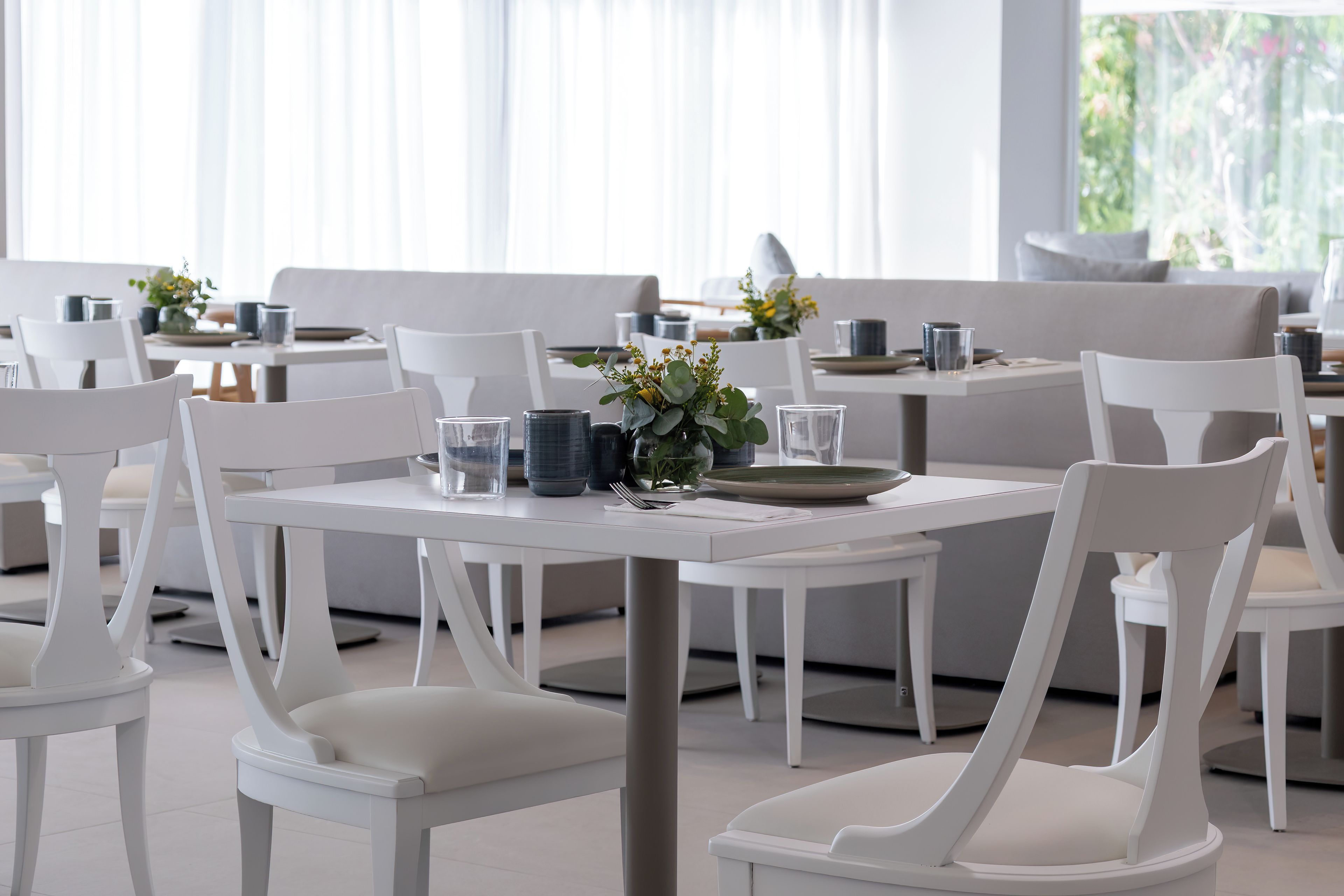 Un comedor moderno con mobiliario blanco y mesas dispuestas para comer.