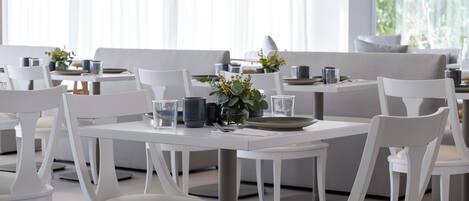 Un comedor moderno con mobiliario blanco y mesas dispuestas para comer.