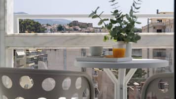Un balcón con planta en maceta, una mesa y vistas de un paisaje urbano con edificios y una montaña.