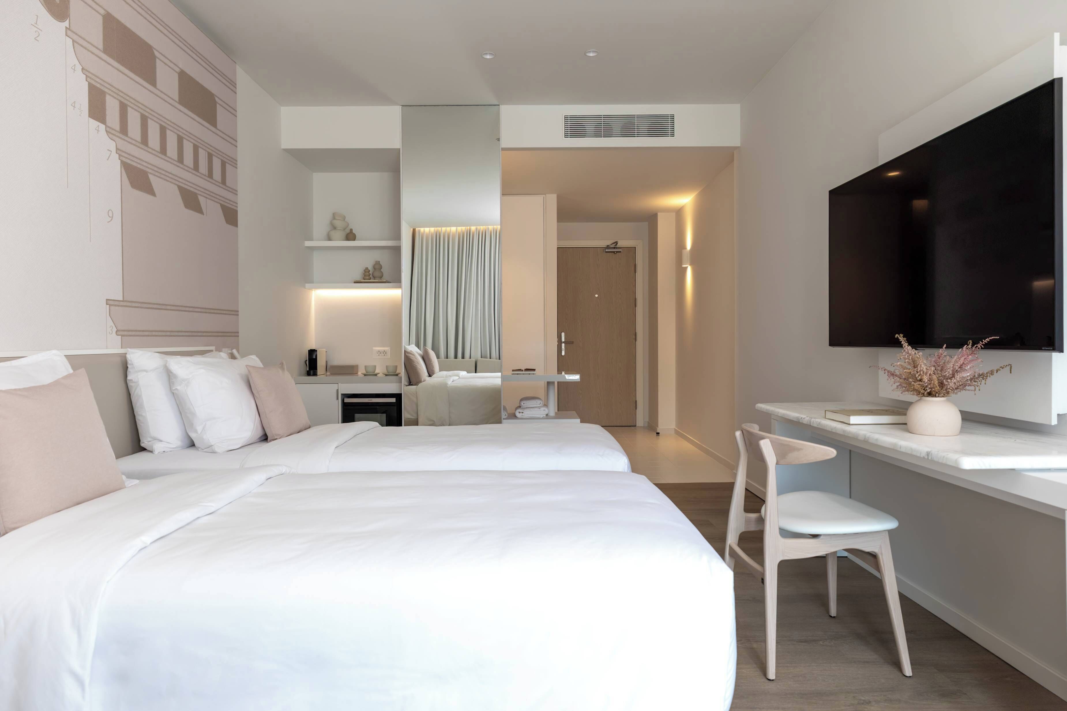 Habitación de hotel moderna con una cama grande, un escritorio, una silla, un televisor y un baño visible a través de una puerta abierta.