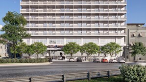 Un edificio de varios pisos con una serie de balcones, cielo despejado y algunos coches estacionados adelante.