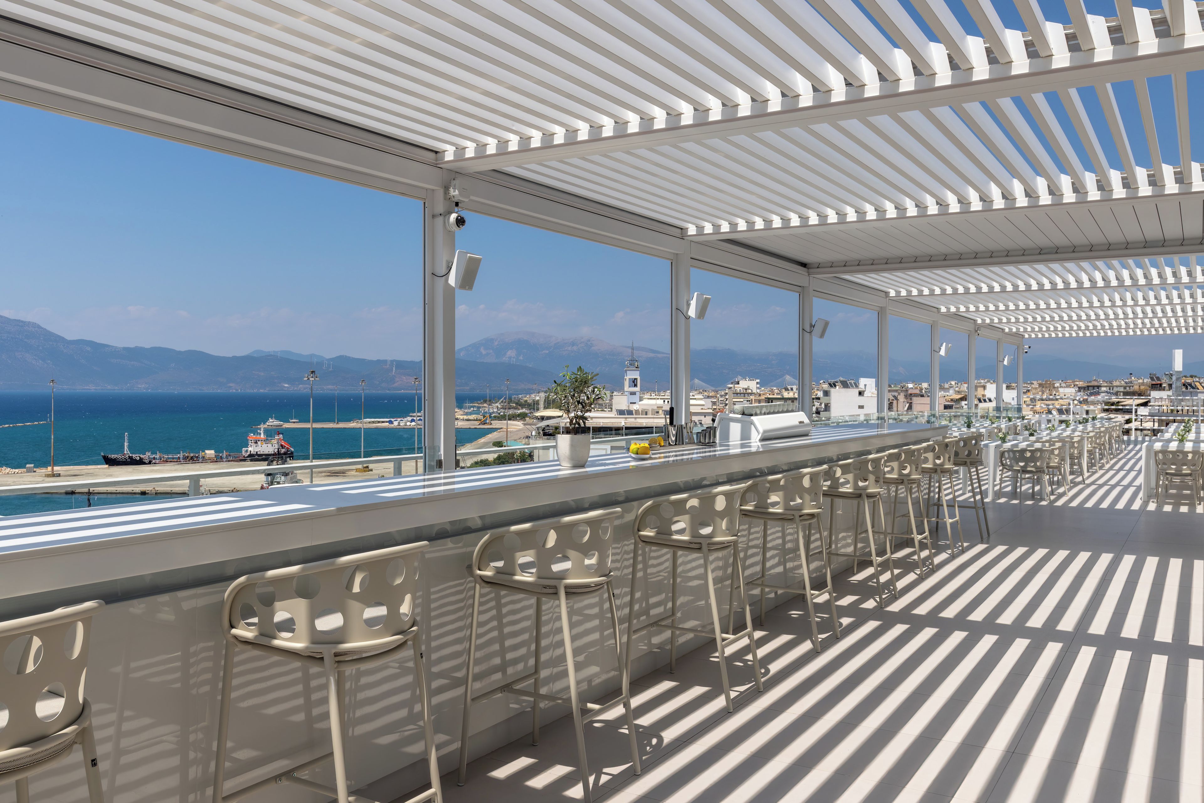 A covered outdoor seating area with a view of the sea and mountains.