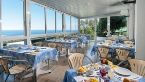 Un restaurante con terraza, mesas cubiertas con manteles azules y vista al mar.