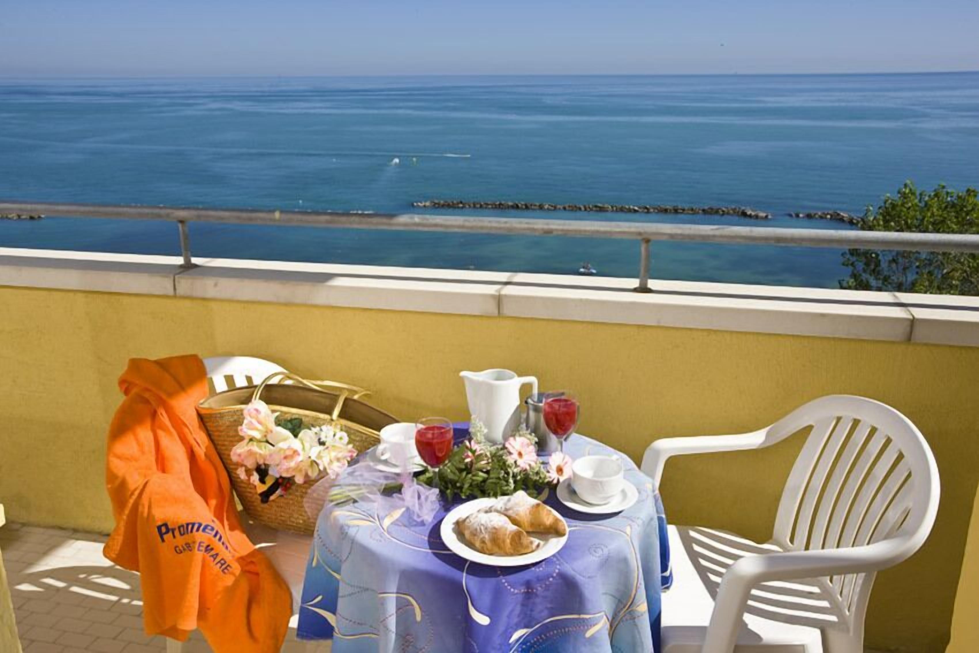 A table set with a croissant, a pitcher, and glasses of red drink, overlooking a coastal view.