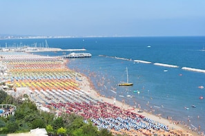 A beach with rows of umbrellas and sun loungers, a pier, and boats in the water. - Hotel Promenade (Gabicce Mare)
