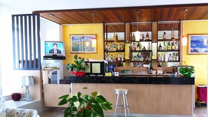 Una sala de estar moderna con techo de madera, una zona de bar con diferentes botellas, un televisor y una planta grande.