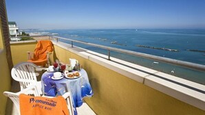 Un balcón con una mesa lista para dos personas, con vista a una playa y una perspectiva despejada del océano y un muelle.