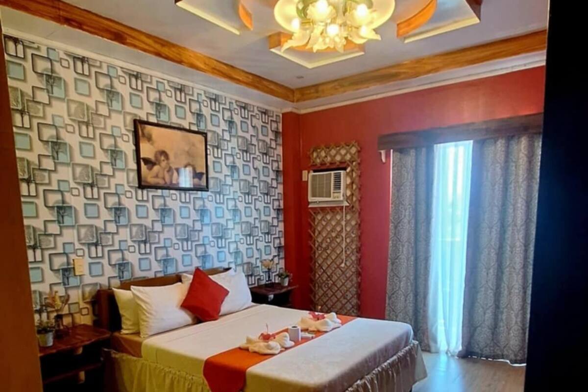 A hotel room with a large bed, a patterned wall, a chandelier, and a view of the outdoors.