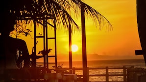 A sunset view from a beachside location with a wooden structure and a palm tree. - Pagudpud Rinnovati Beach Resort (Pagudpud)