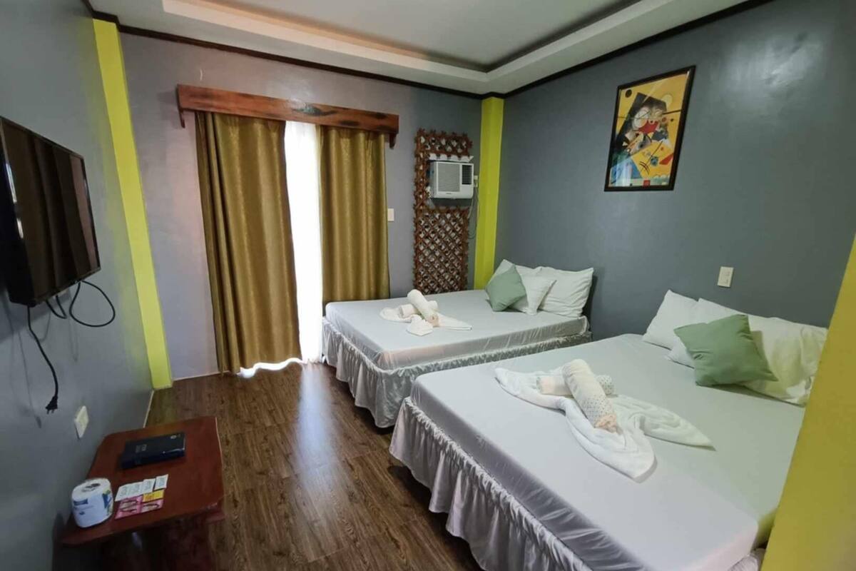 A hotel room with two beds, a TV, a desk with a phone and a lamp, and a window with curtains.