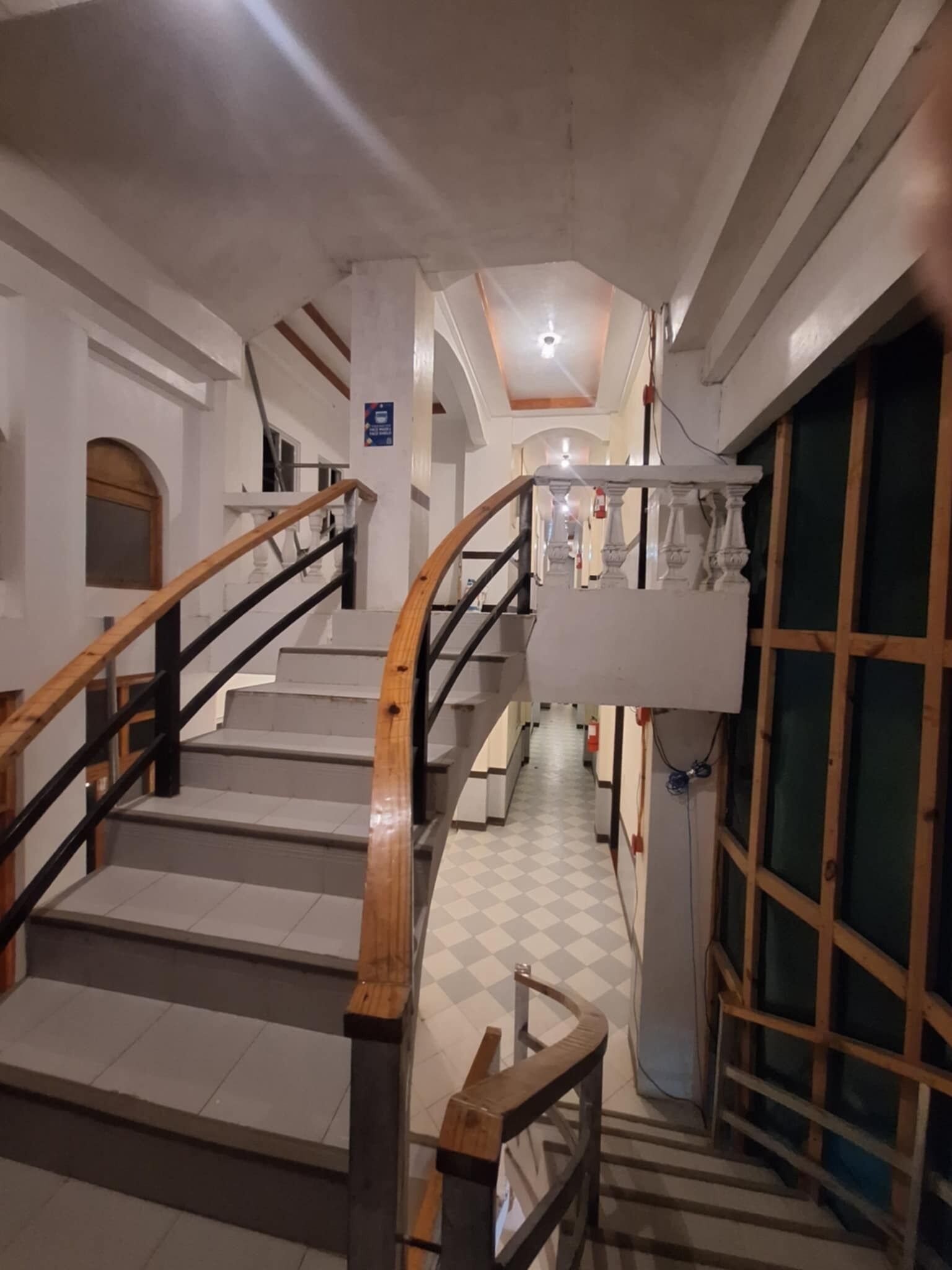 A staircase with wooden railings and a checkered floor leading to a room with a green window.