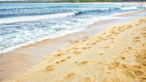 A beach with footprints in the sand, waves, and a distant view of wind turbines and hills. - Pagudpud Rinnovati Beach Resort (Pagudpud)