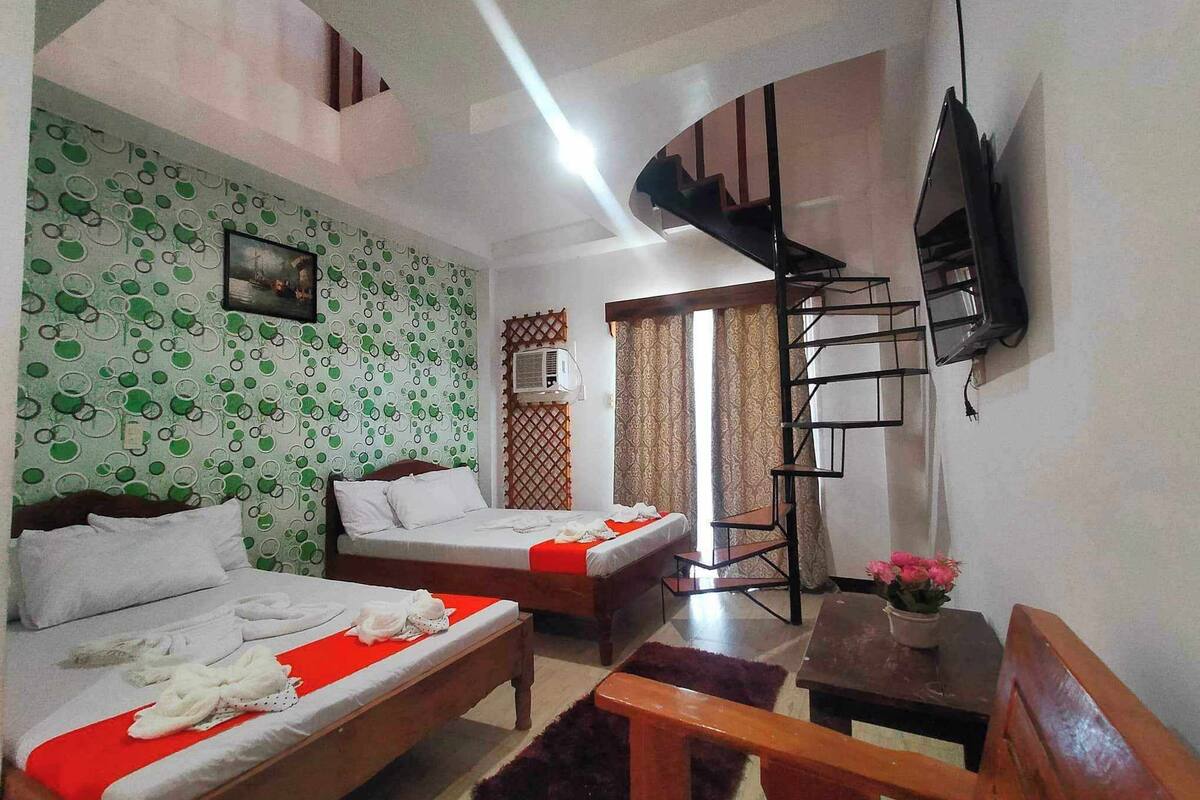 A hotel room with two beds, a TV, a staircase, and a window with curtains.