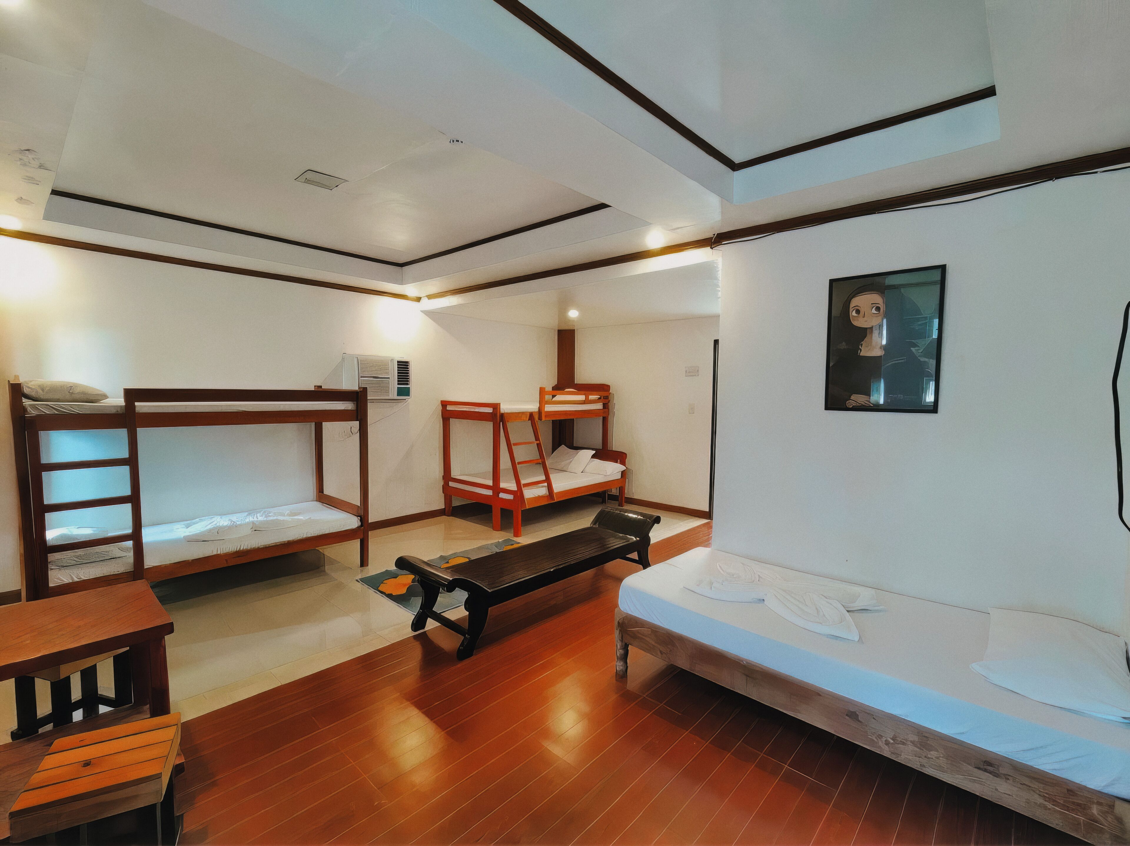A dormitory room with bunk beds, a desk, and a bench.