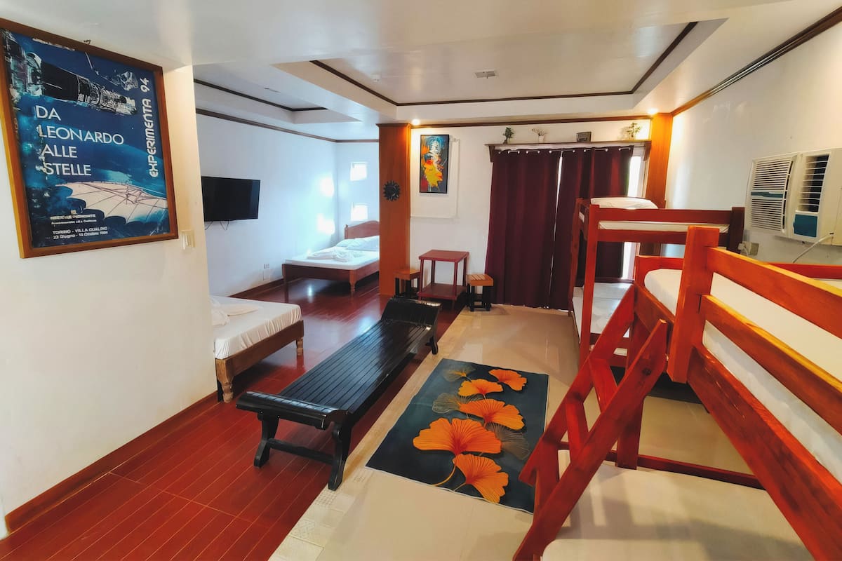 A hotel room with a bed, a bench, a small table, and a wooden staircase.