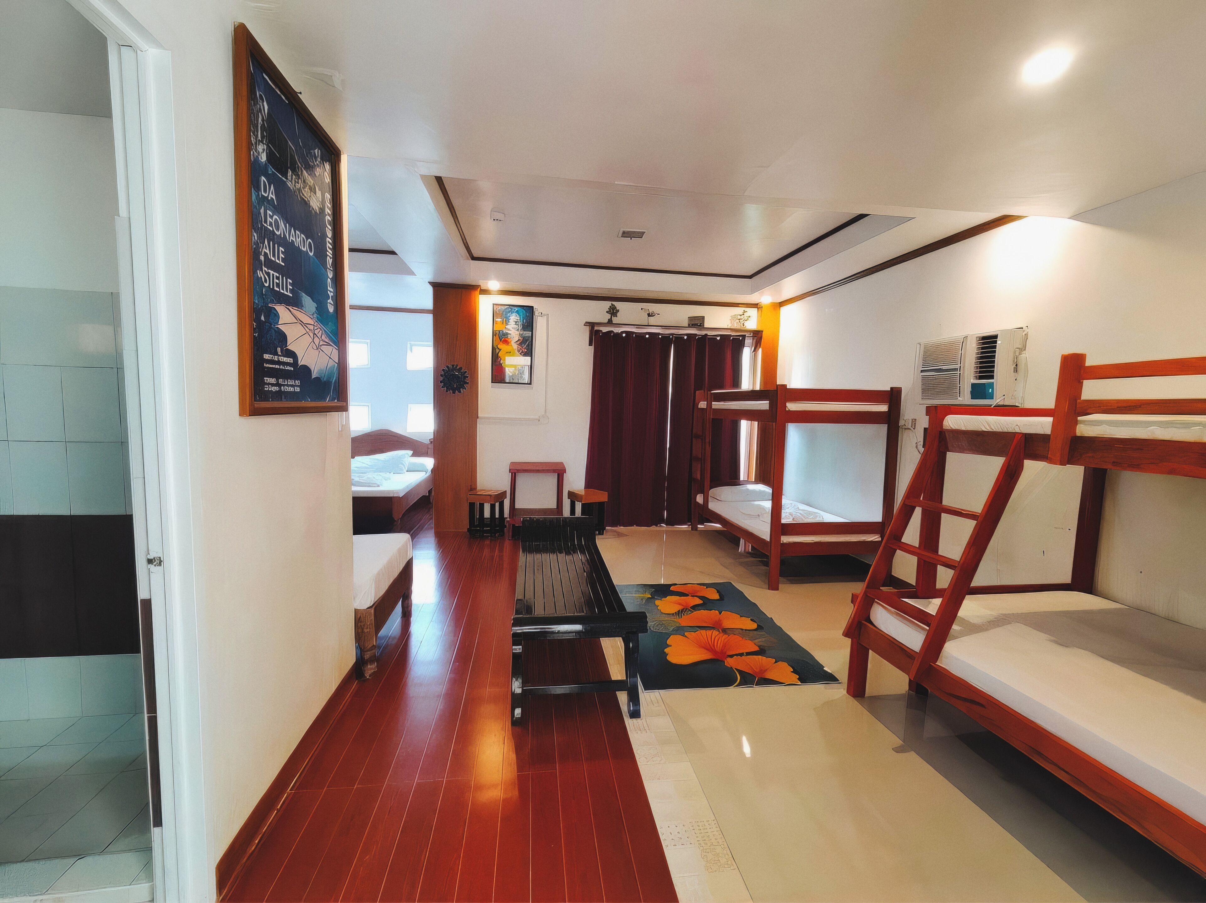 Habitación de hotel pequeña con piso de madera, literas, un escritorio y una cama con cabecera.
