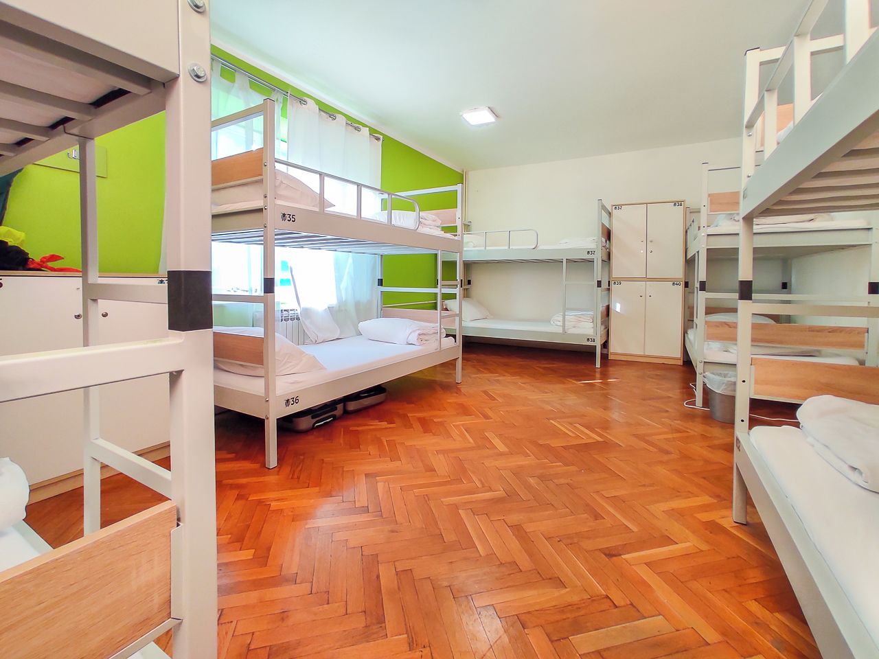 A dormitory room with bunk beds, wooden flooring, and a green accent wall.
